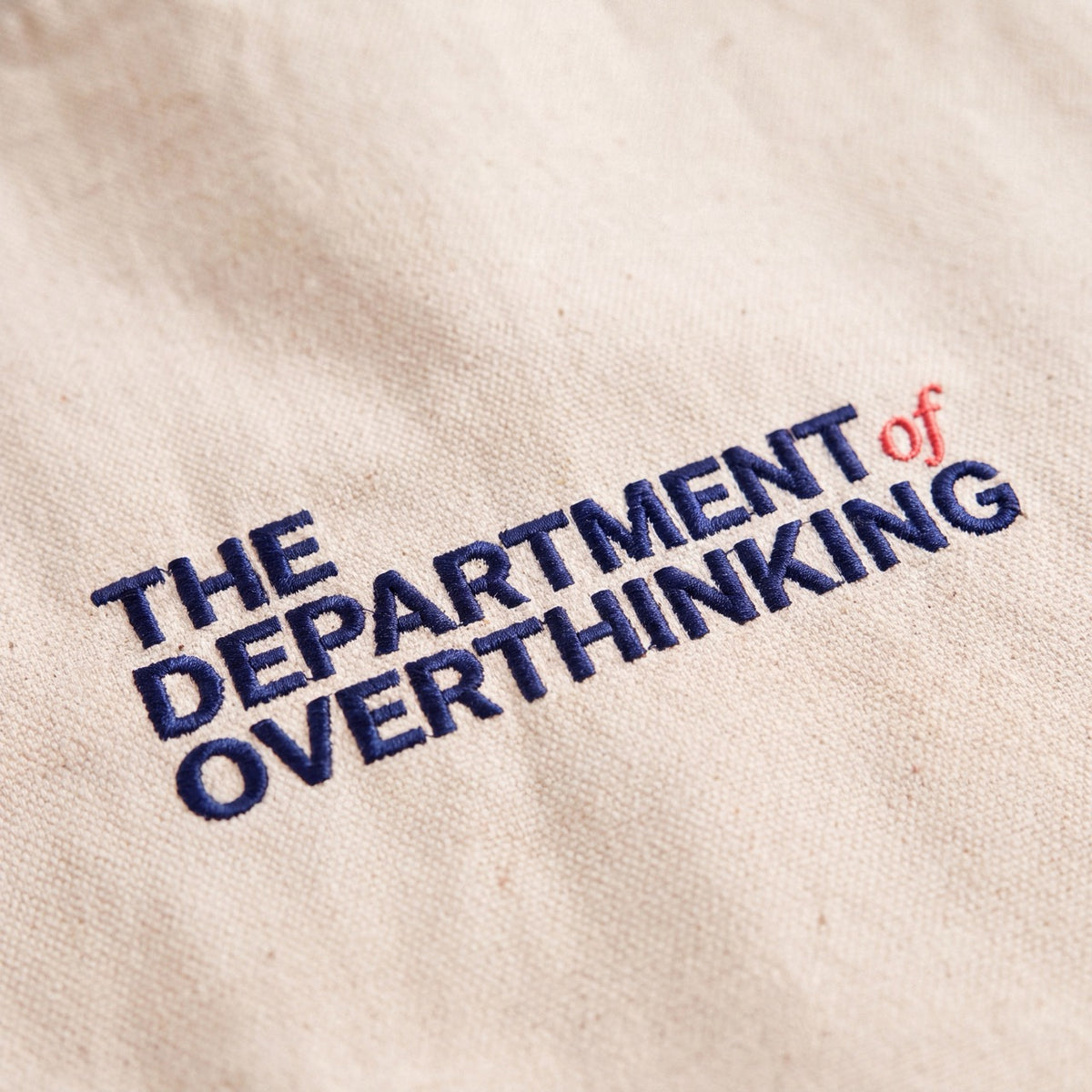 Close-up of cream Department of Overthinking embroidery on navy recycled cotton tote bag