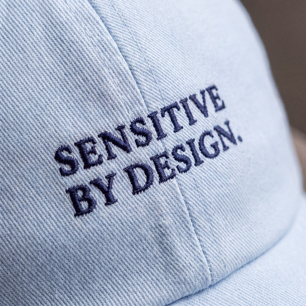 Close-up of SENSITIVE BY DESIGN. embroidery on light blue cap