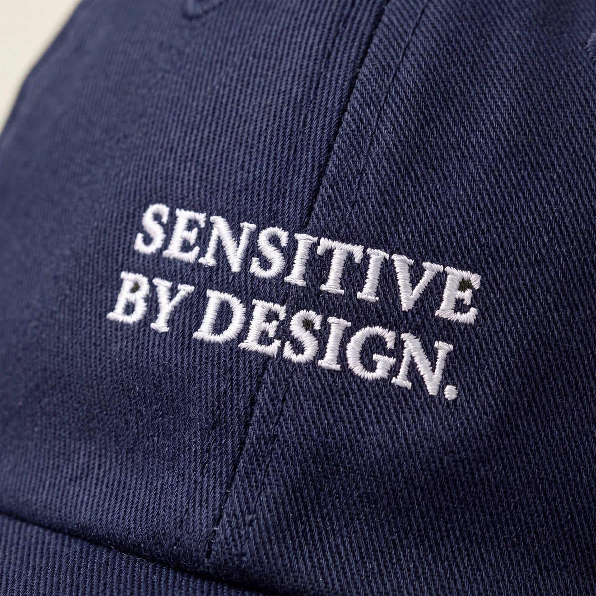 Close-up of SENSITIVE BY DESIGN. embroidery on navy cap
