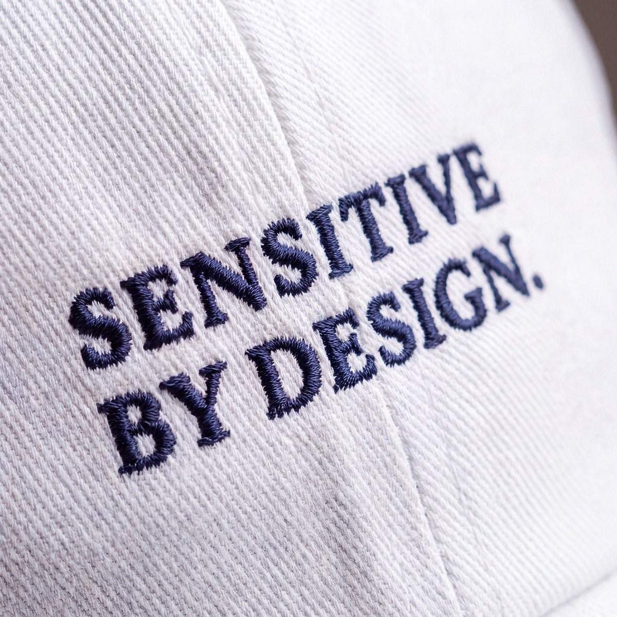 Close-up of SENSITIVE BY DESIGN. embroidery on white cap
