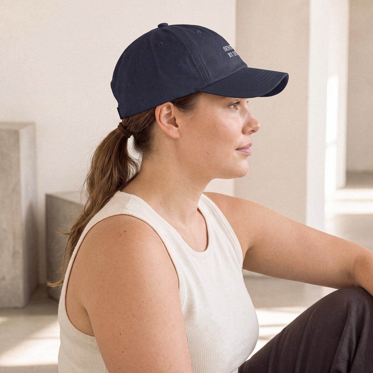 Side profile of woman wearing a navy Department of Overthinking cap