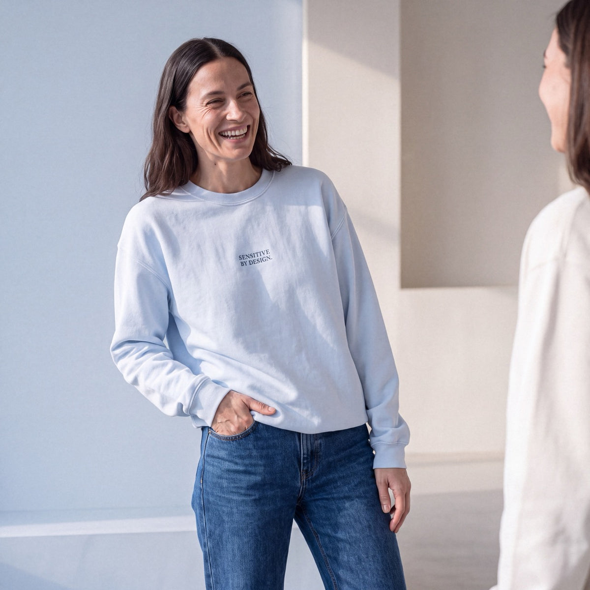 Front view of woman wearing a light blue SENSITIVE BY DESIGN. sweatshirt