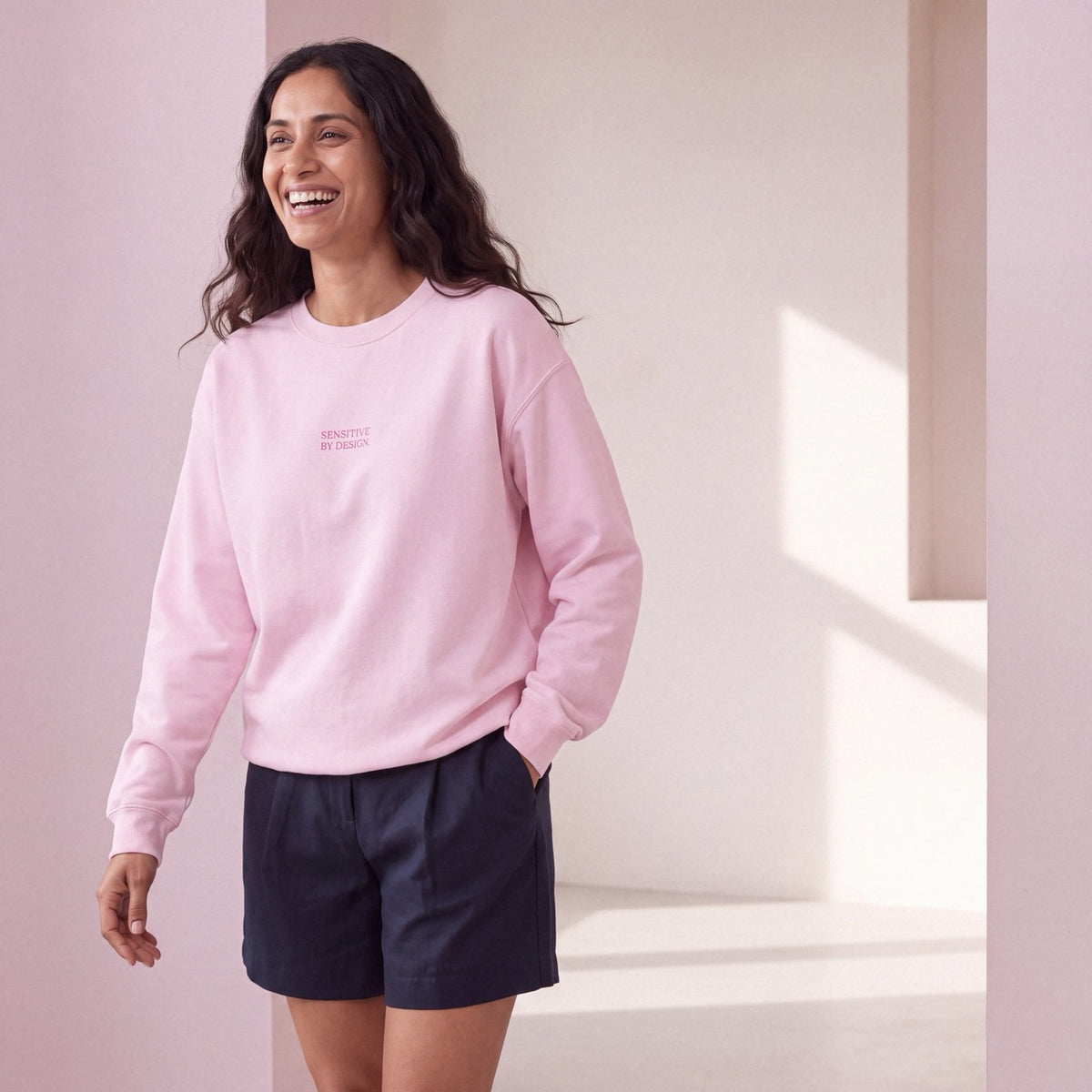 Front view of woman wearing a light pink SENSITIVE BY DESIGN. sweatshirt