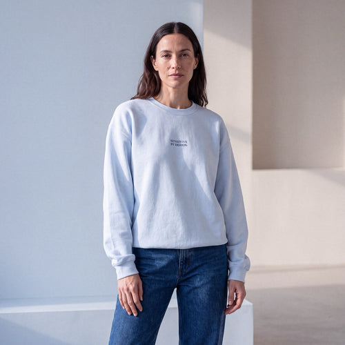 Woman wearing a light blue SENSITIVE BY DESIGN. embroidered crewneck sweatshirt