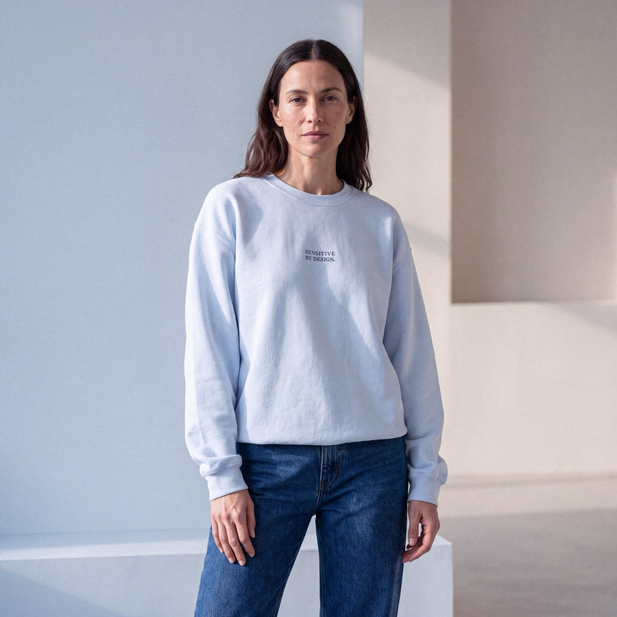 Woman wearing a light blue SENSITIVE BY DESIGN. embroidered crewneck sweatshirt