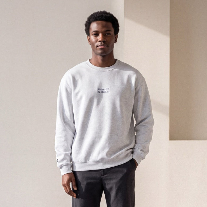 Man wearing an ash SENSITIVE BY DESIGN. embroidered crewneck sweatshirt
