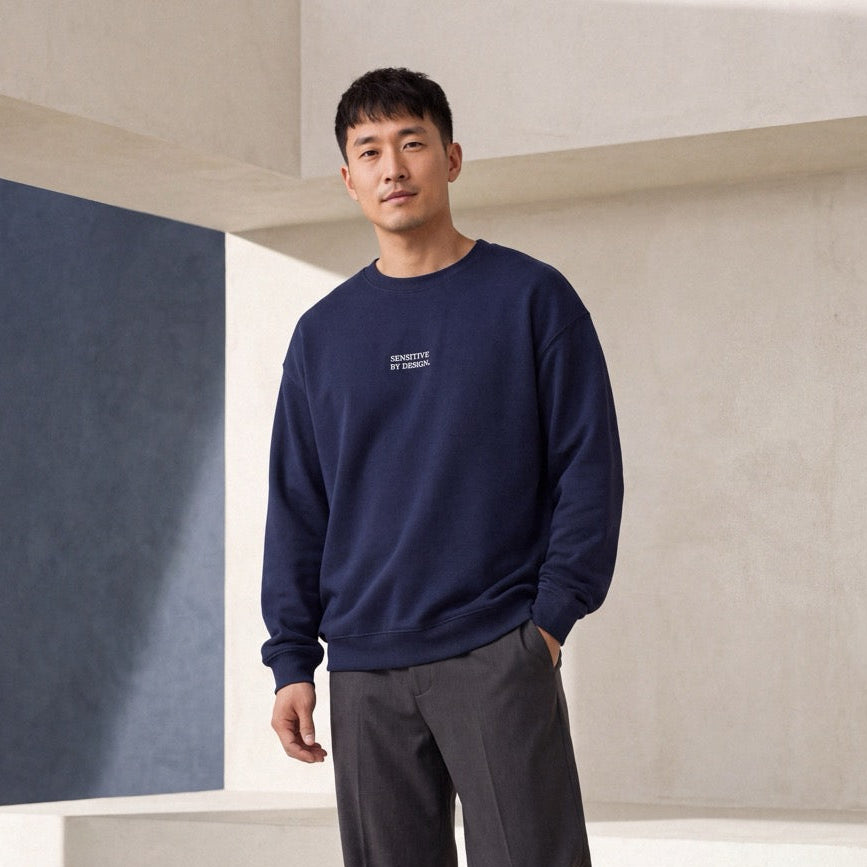 Man wearing a navy SENSITIVE BY DESIGN. embroidered crewneck sweatshirt