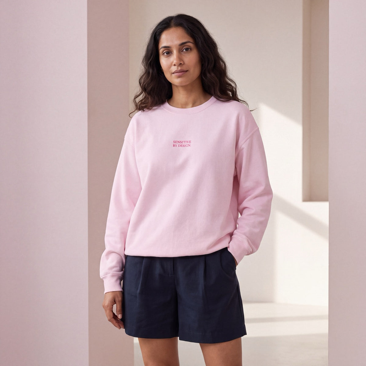 Woman wearing a light pink SENSITIVE BY DESIGN. embroidered crewneck sweatshirt