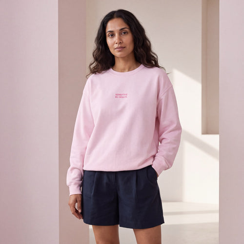 Woman wearing a light pink SENSITIVE BY DESIGN. embroidered crewneck sweatshirt
